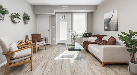 An open living room with a couch, coffee table and two chairs. set next to a patio door with window, with a long tall window next to it