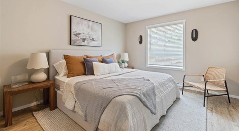 A large bright bedroom with queen sized bed, night stands and a chair.