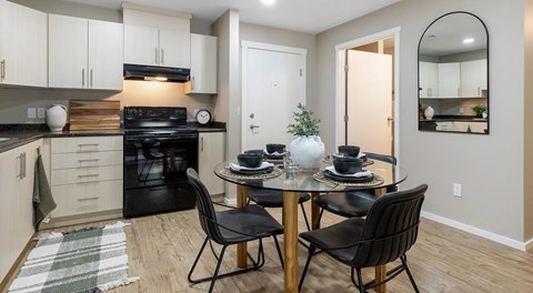 A bright kitchen with light cabinets and black appliances, a round table sits in the centre with four chairs