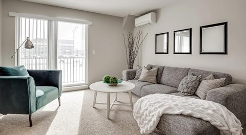 A living room with a sectional, coffee table and chair. A glass sliding door with lots of natural light