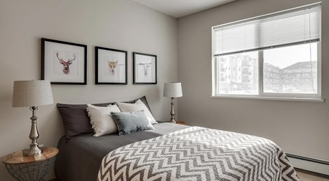 A bedroom with large bed, nightstands and large window with blinds