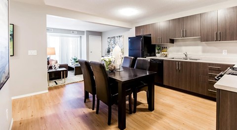 An apartment kitchen with dark cabinets and light counter tops, black appliances and a table set for four