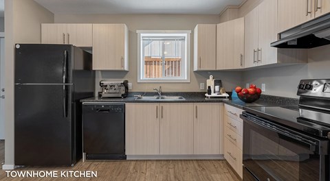 Townhome kitchen with light cabinets and black appliances. A window sits between the cabinets above the sink