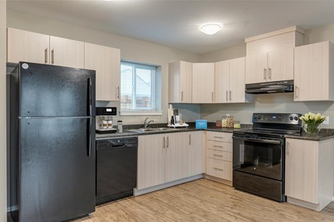 A black refrigerator is in a kitchen with wooden floors and cabinets.
