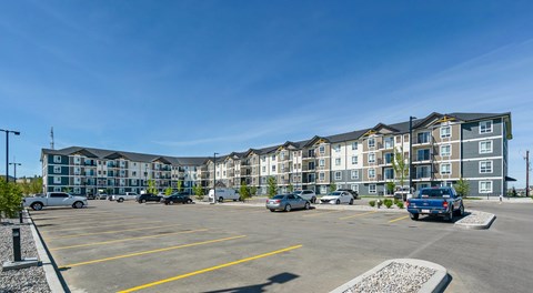 A large L shaped apartment building with a parking lot in front