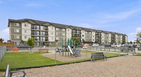 A large four storey apartment building with parking and a playground out front.