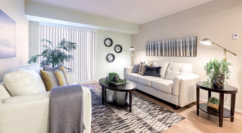 A living room with a couch and chair separated by a coffee table in the centre. large glass door with blinds in front