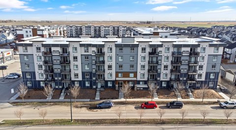 A large apartment complex with a parking lot behind the buildings and street parking out front