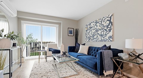 A blue couch sits in a living room with a glass table and a large abstract painting on the wall.