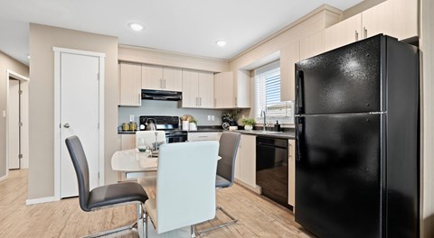 A black refrigerator stands in a kitchen with a white table and chairs.