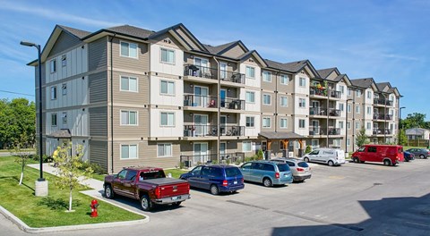 A row of apartment buildings with cars parked in front.