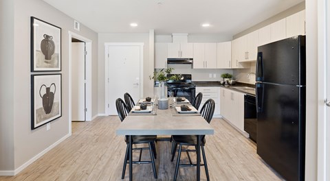 A bright open kitchen with light cabinets, black appliances and a rectangular table set for four