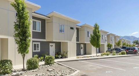 A row of modern townhouses with a parking lot in front.