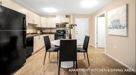 An apartment kitchen with light cabinets, black appliances and a kitchen table in the centre