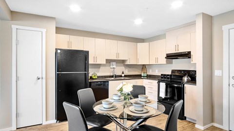 A modern bright kitchen with light cabinets, black appliances, a pantry and kitchen table set for four