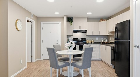 A modern bright kitchen with light cabinets and black appliances. a round table sits in the centre.