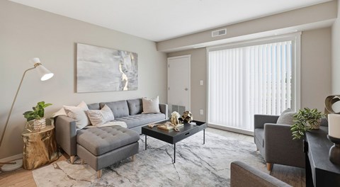 A modern living room with a small sectional, coffee table, and chairs. A large glass sliding door on the exterior