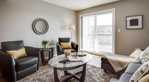 A living room a small sectional, coffee table and two arm chairs. A large glass sliding door sits next to them