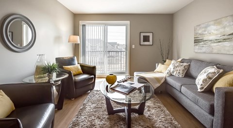 A living room with small sectional, coffee table, two chairs and an end table. A large glass sliding door leading to a balcony on the end