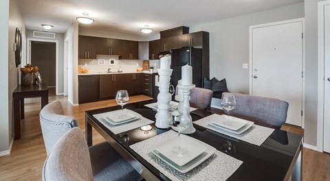 A large open kitchen with dark cabinets and black appliances, across the open kitchen a square kitchen table sits with seating for four