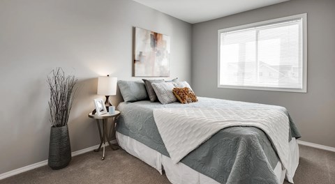 A bedroom with a large bed, nightstand, and large window with blinds.