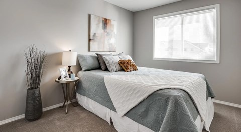 A bedroom with a bed, nightstand, and a large window.