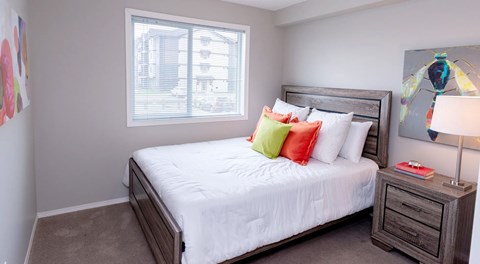 A bedroom with a large bed, nightstand and large window