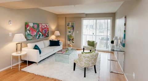 A living room with a couch, coffee table and two arm chairs. A large glass sliding door sits on the outer wall