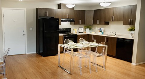 A kitchen with dark cabinets, black appliances and light counters. A square table sits in an opening in the center.