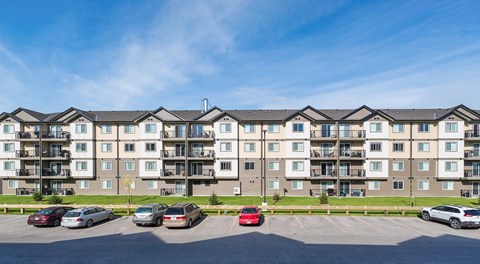 A large apartment building with small green space separating it and a parking lot