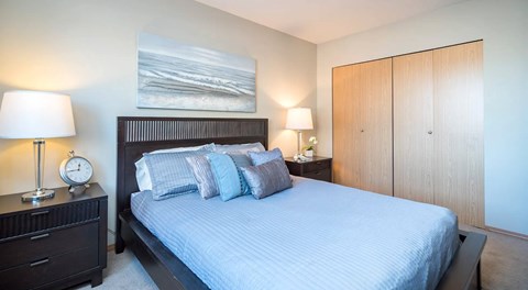 A bedroom with a bed, nightstand, and large closet