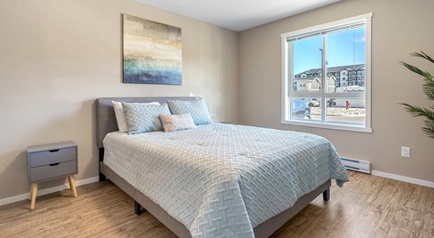 A queen sized bed with nightstands sits in a bedroom with a large window
