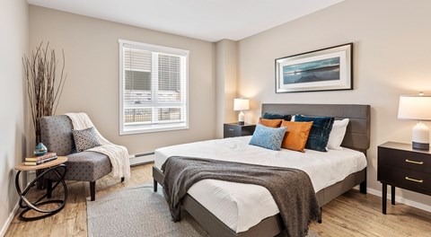 A bedroom with a queen sized bed, a chair, and a nightstand.