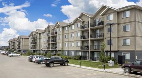 A row of apartment buildings with cars parked in front.