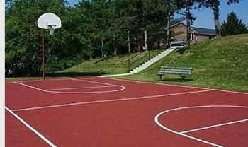 A basketball court with a red surface and white lines, a basketball hoop, and a bench.
