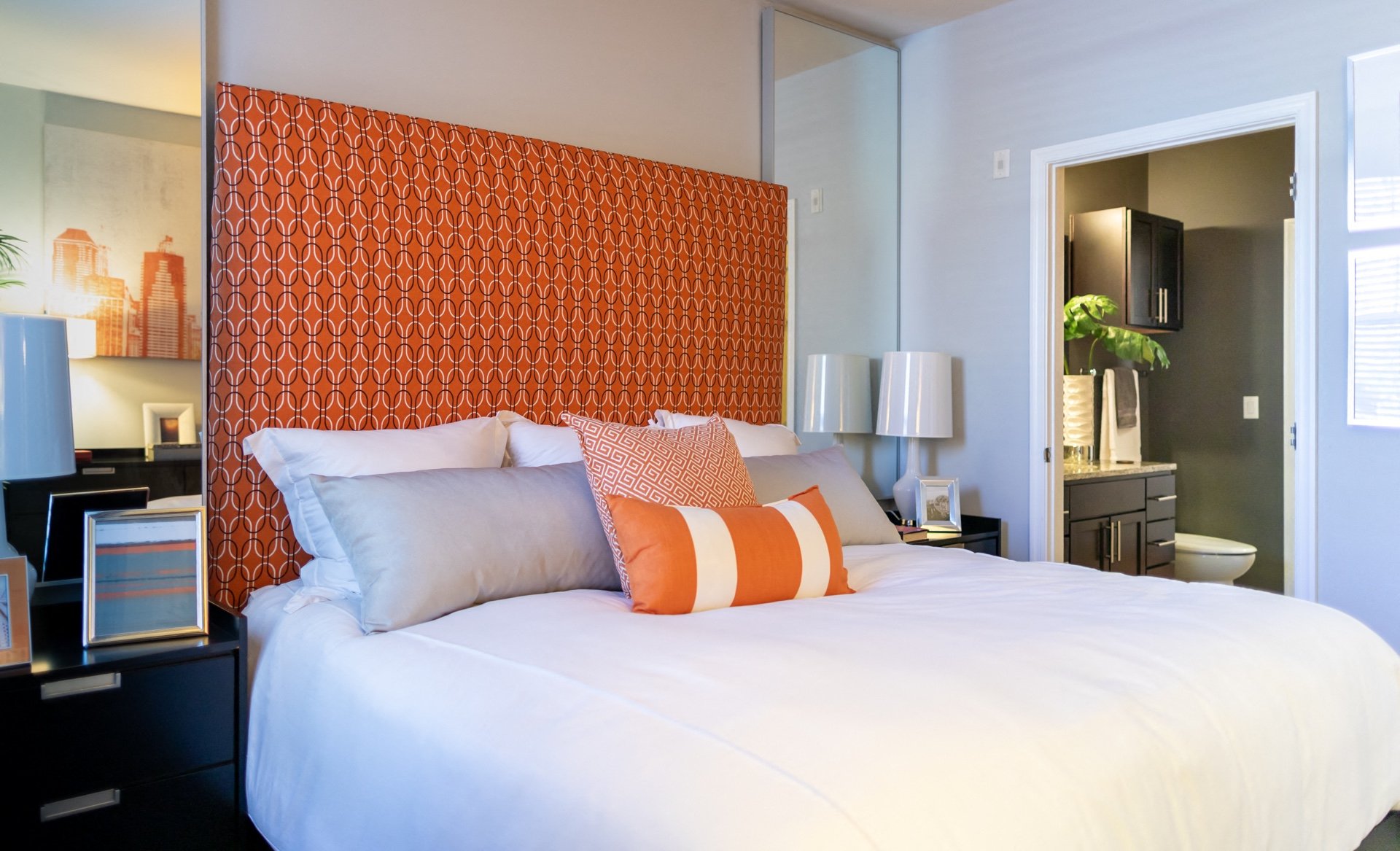A bed with white sheets and orange and white pillows in a bedroom.