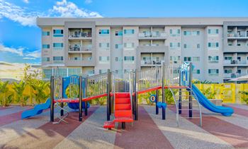 A playground with a red slide and a blue slide in front of a building.