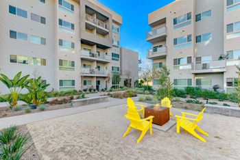 A sandy area with yellow chairs and a fire pit in front of apartment buildings.