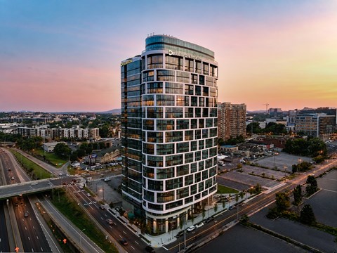 A tall, modern building with many windows is surrounded by a busy road with cars.