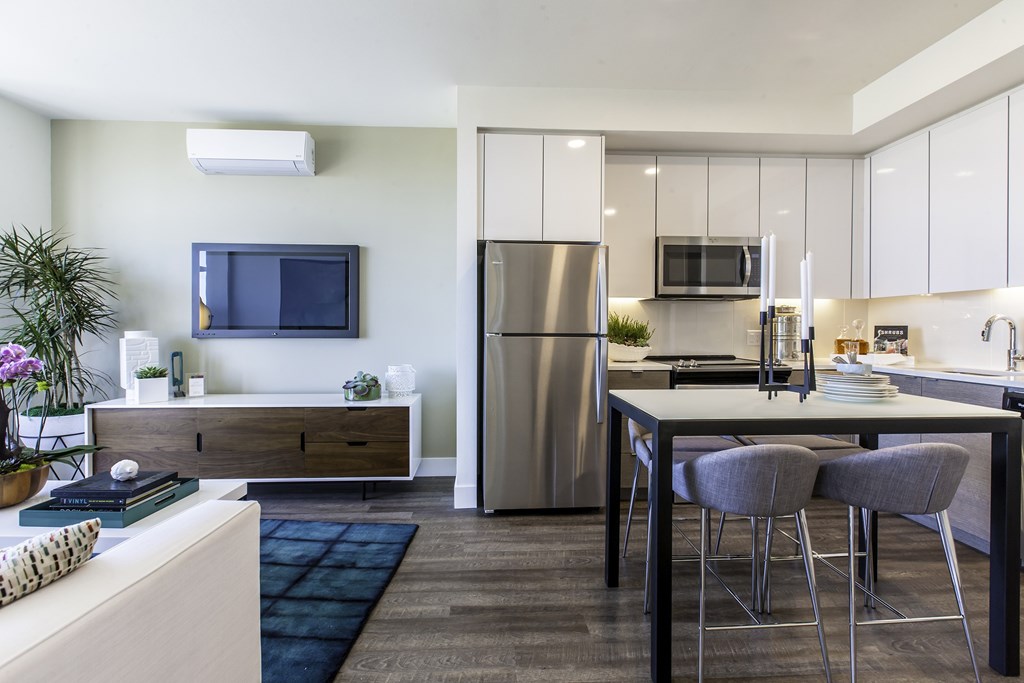 A modern kitchen with a refrigerator, microwave, and a dining table with chairs.