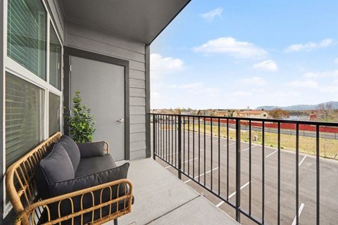 A balcony with a black railing and a wicker chair with cushions.