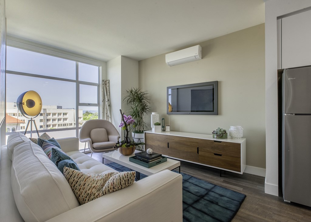 A modern living room with a white sofa and a flat screen TV mounted on the wall.