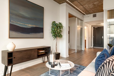 A living room with a painting on the wall and a plant on the side table.