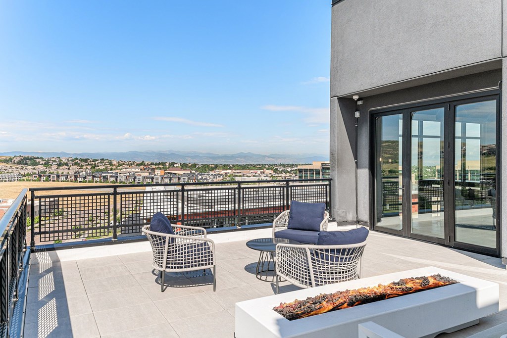 A balcony with two chairs and a table with a fire pit on it.