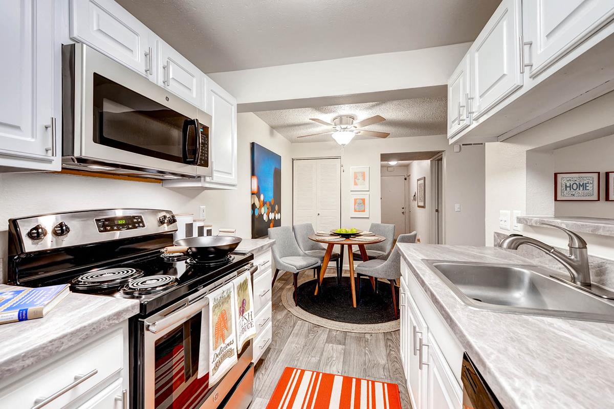 Kitchen with White cabinetry, light grey countertops and appliances including dishwasher, stove, oven and microwave