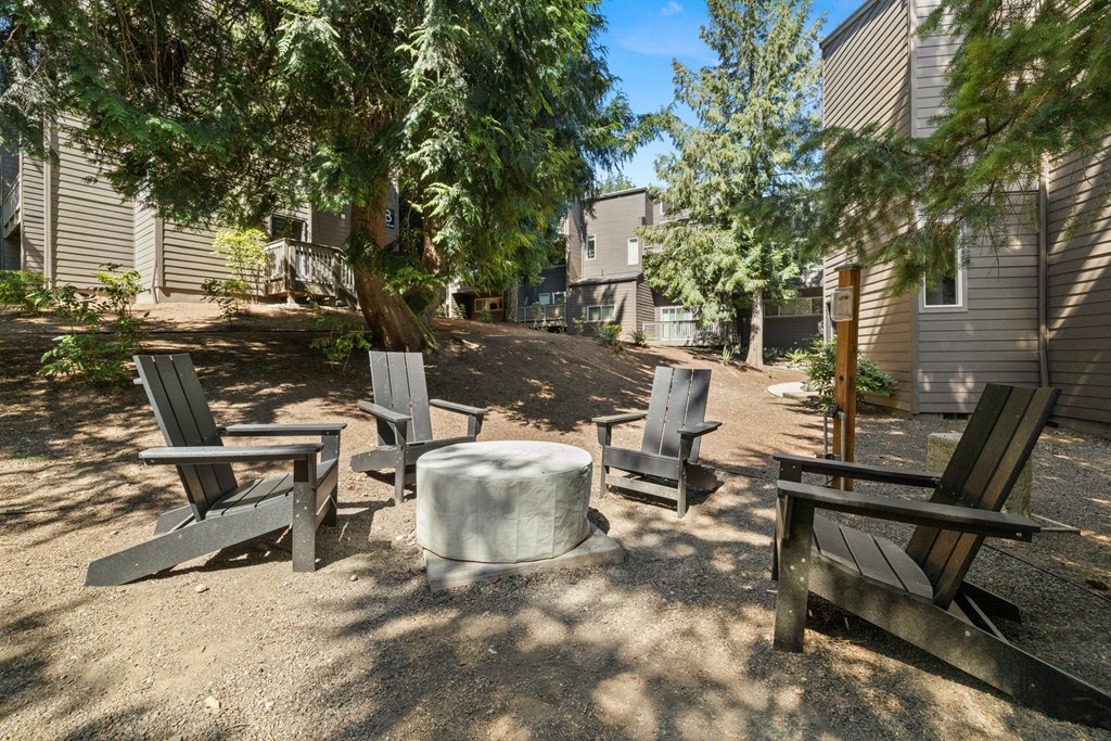 a firepit with four chairs and a table in the middle of a dirt area with trees  at Larkspur West Linn, Oregon