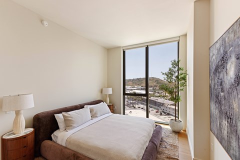 A bedroom with a large bed and a view of the city outside the window.