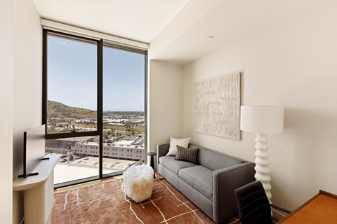 A living room with a grey couch and a large window overlooking a city.