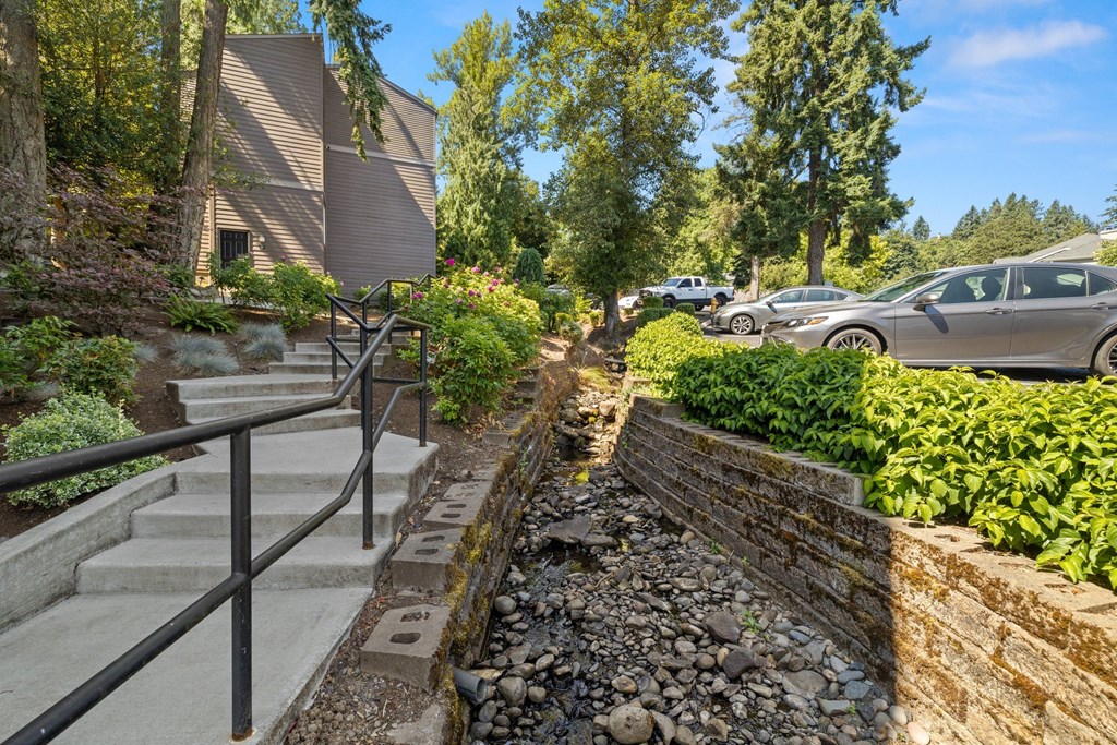 a creek running through a yard with a stone retaining wall and a stone wall with bushes and at Larkspur West Linn, West Linn, OR, 97068