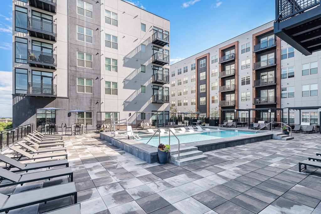 A large outdoor pool area with sun loungers and a building in the background.